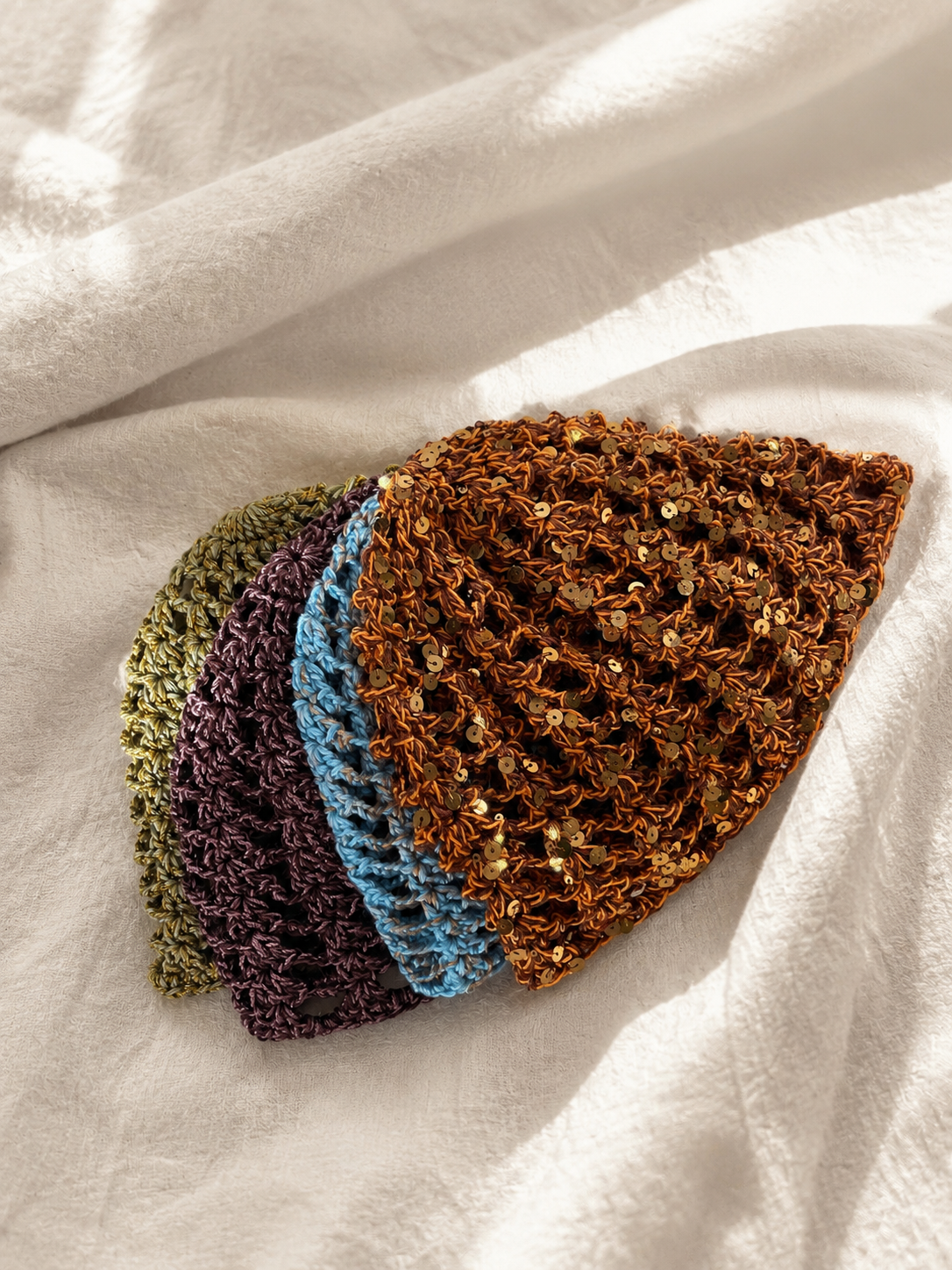 Three crocheted hats in green, purple, and brown on a white fabric background